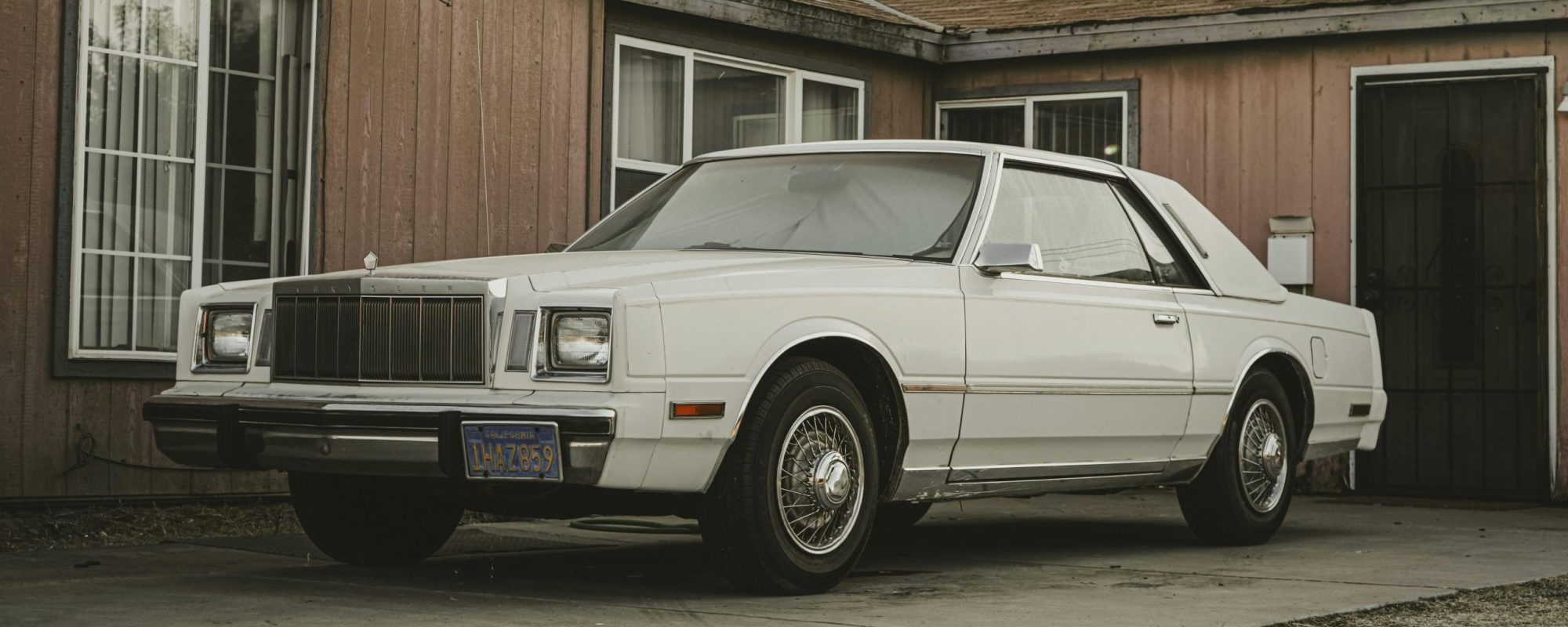 Classic white Chrysler Cordoba parked in front of a retro house with vintage style.