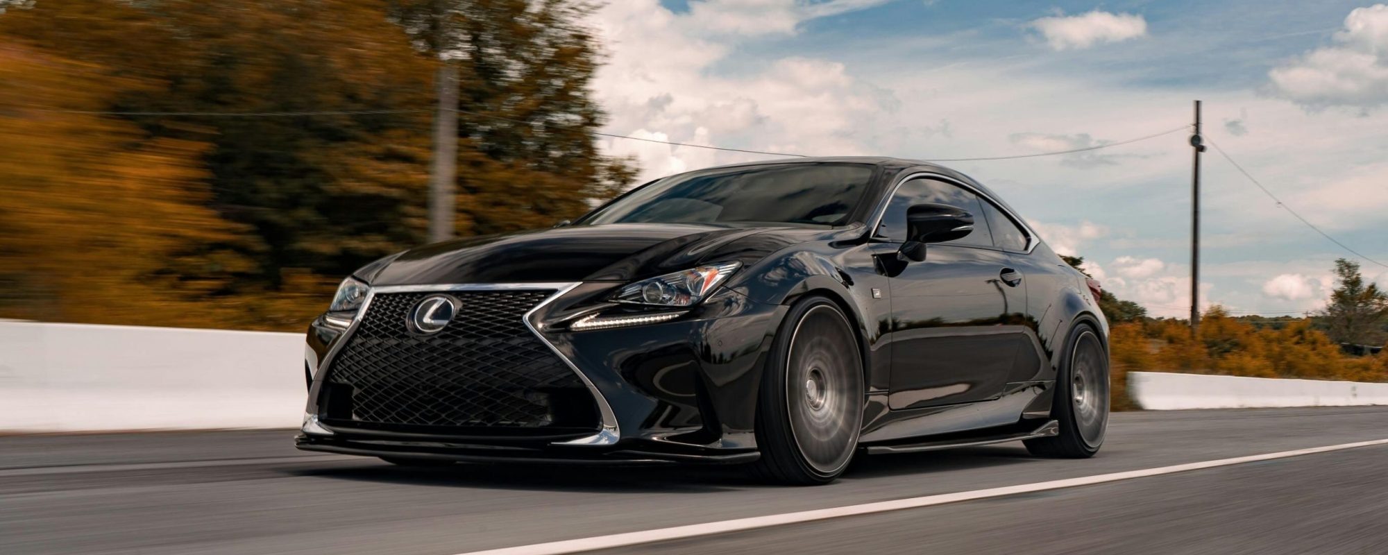 A black Lexus car driving swiftly on an open road amidst scenic landscapes and clear skies. Lexus Spacers & Adapters